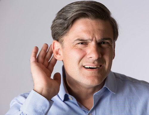 A man with his hand next to his ear trying to hear