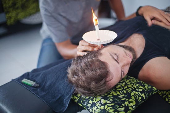 Man lying down receiving ear candling treatment