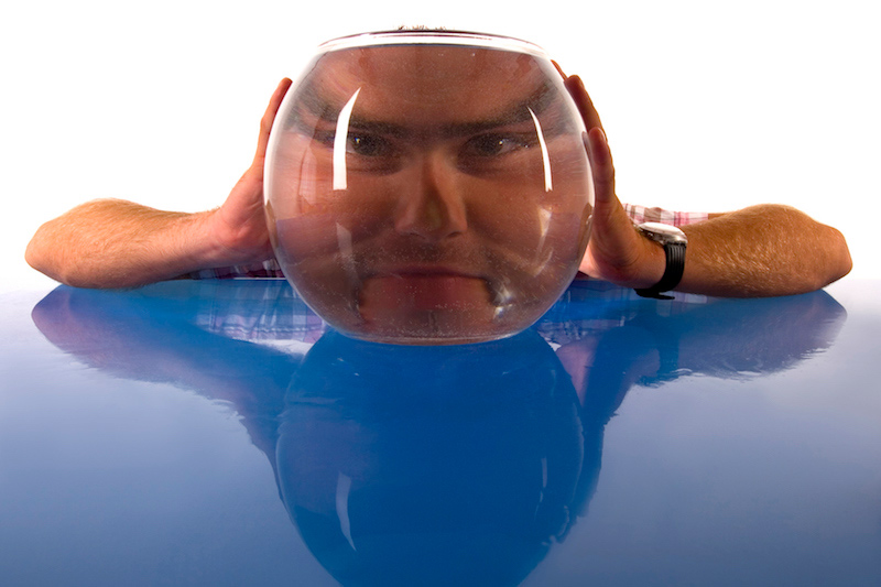 Man with his face behind a fish bowl looking distorted.