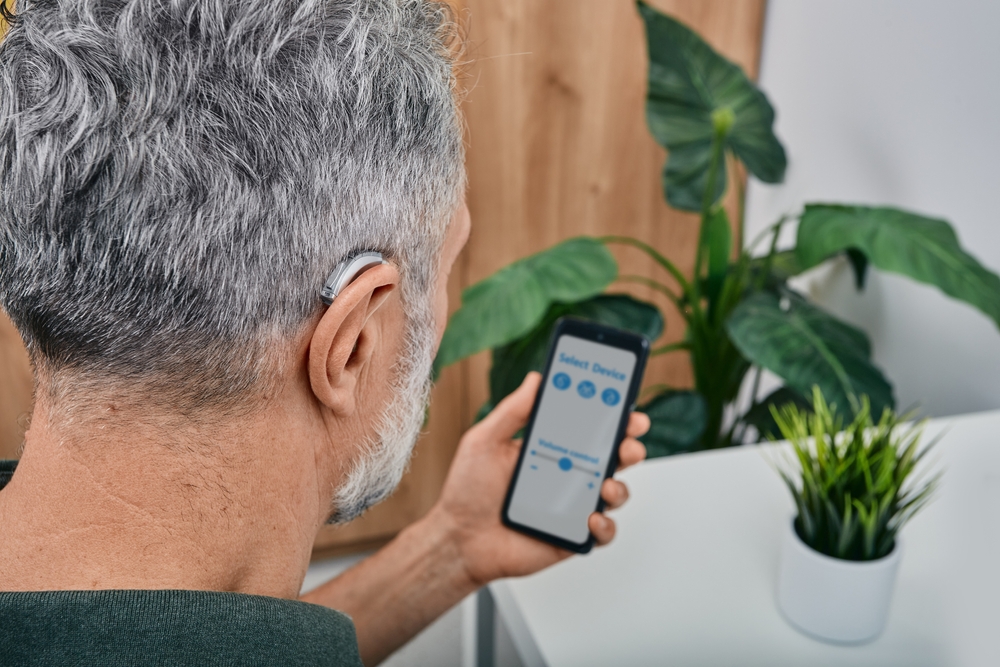 mature man adjusts settings for his BTE hearing aid via smartphone.