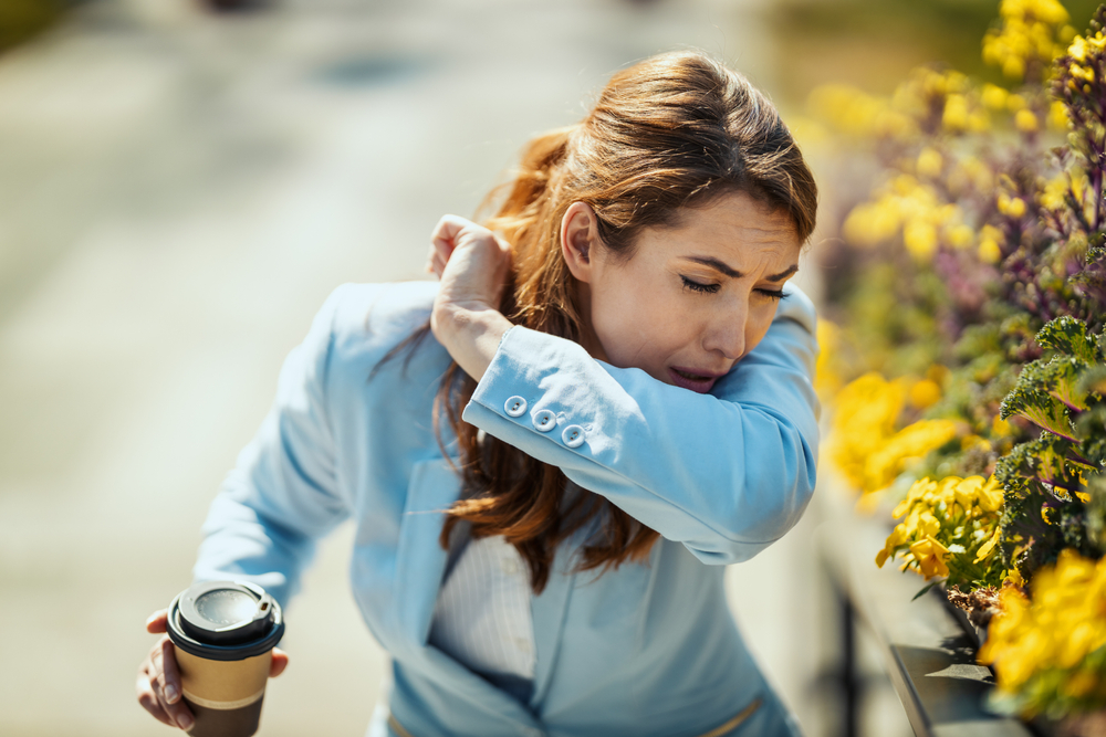 woman outside sneezing into elbow.