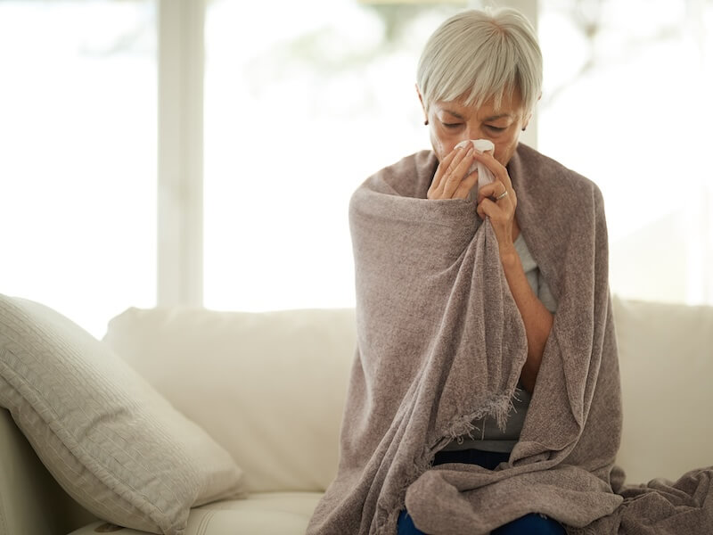 senior woman blowing her nose with a tissue at home.