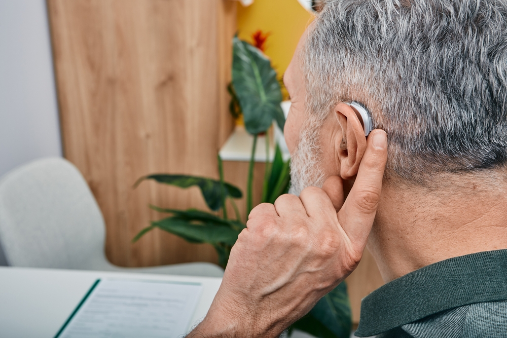 man tunes his hearing aid behind the ear.