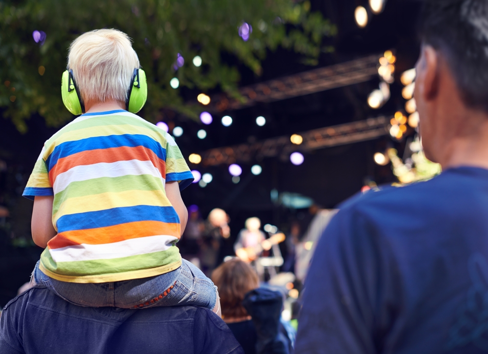 Rearview shot of a young boy with hearing protection sitting on his fathers shoulders at a music concert.