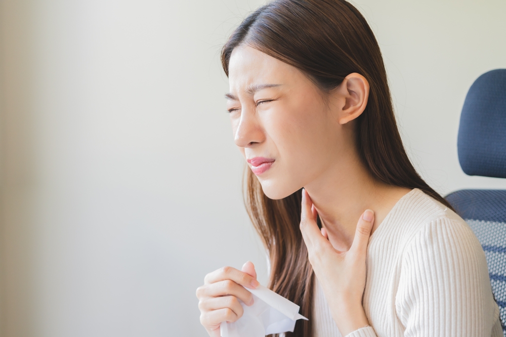 woman touching her neck due to post-nasal drip and holding tissue.