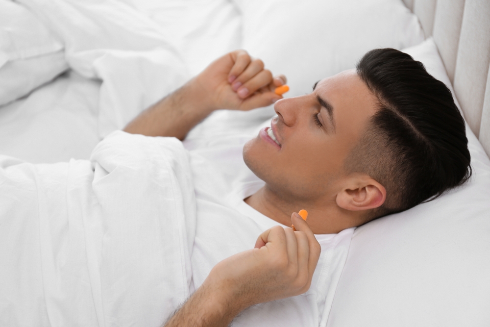 Man inserting foam ear plugs in bed.