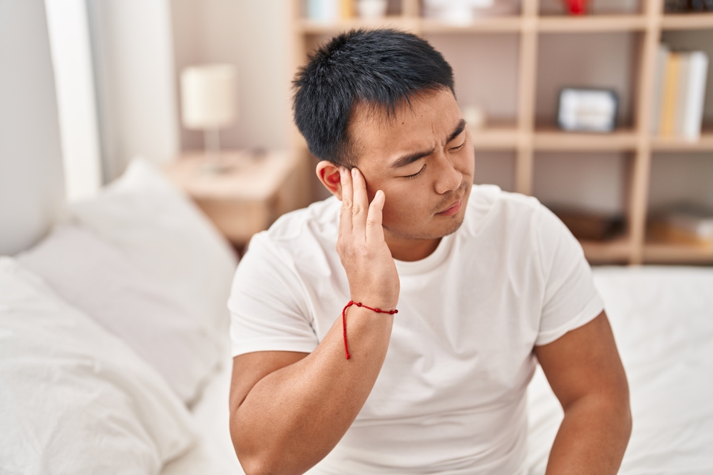 asian man suffering from ear pain at home.