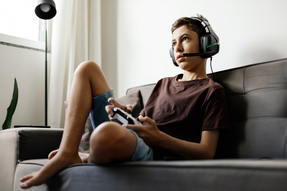 teenage boy playing video game on the couch with headphones on.