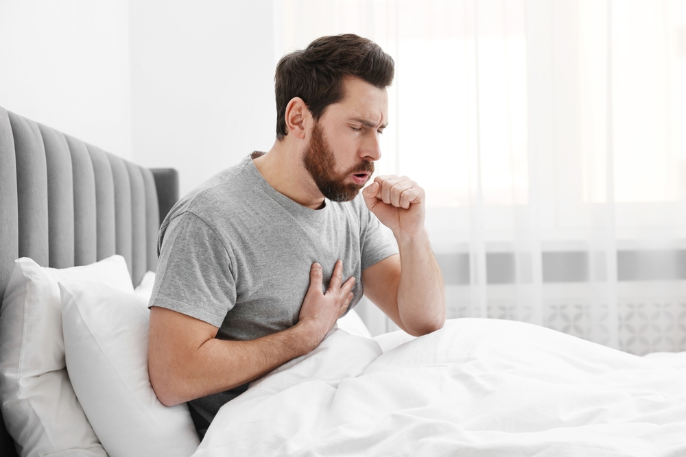 man coughing in bed at home.