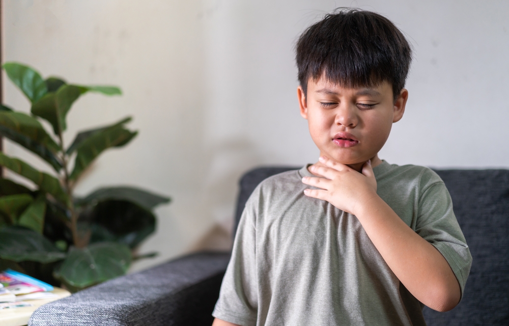 Sick boy touching his neck due to throat pain.