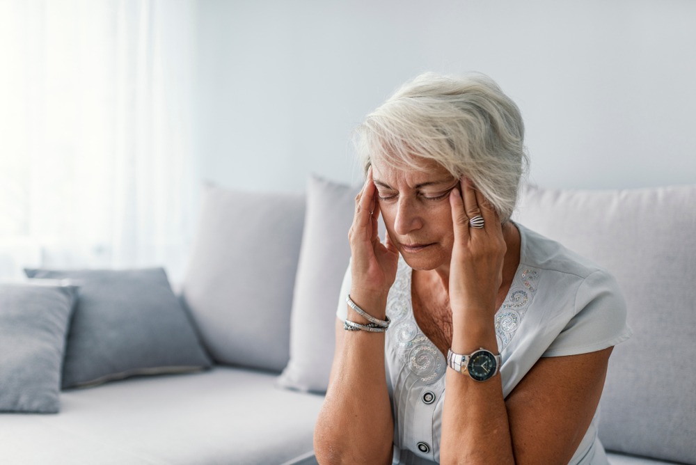 mature woman suffering from headache at home on sofa.