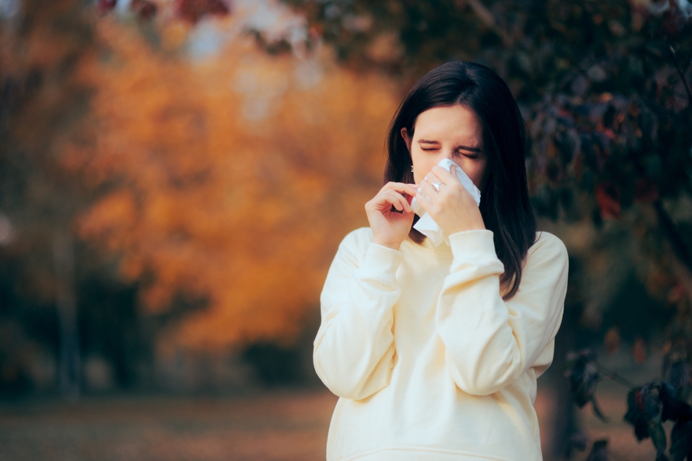 woman outside blowing her nose during autumn.