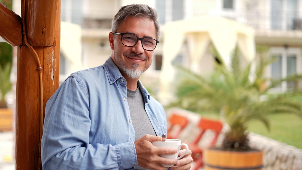 happy middle aged man at home outdoor on terrace in garden, relaxing, drinking morning coffee.