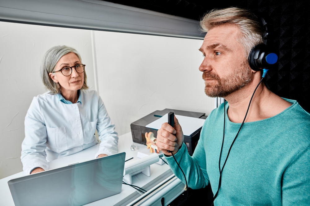 Male patient wearing audiology headphones pressing button of response while audiometric testing in soundproof audiology booth.