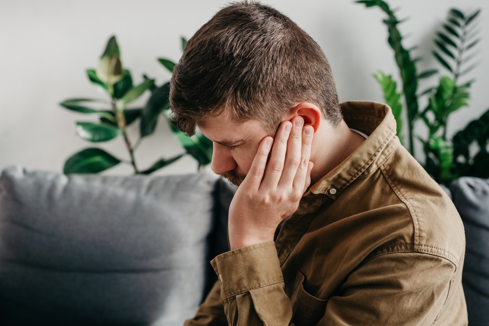 sick man sitting down with ear pain at home.