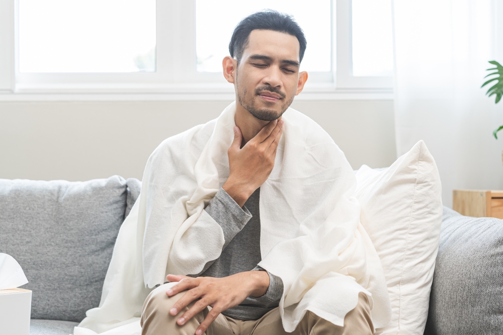 man sick sitting on couch with a sore throat.