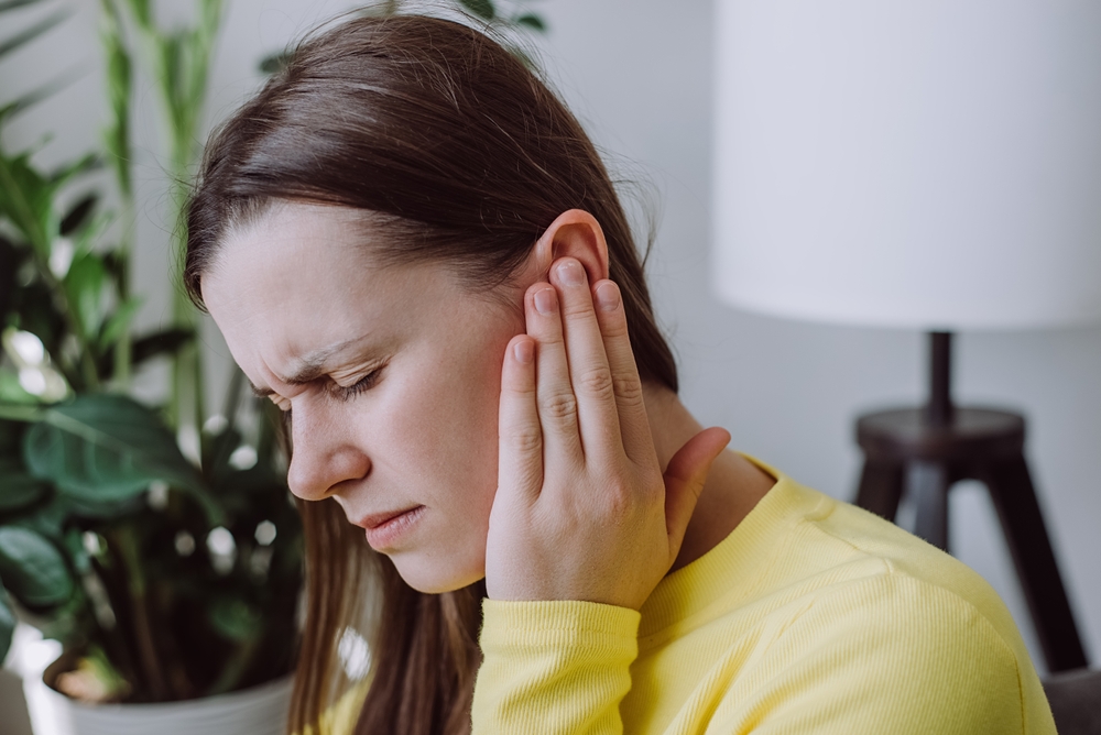 woman in yellow shirt holding ear due to pain.