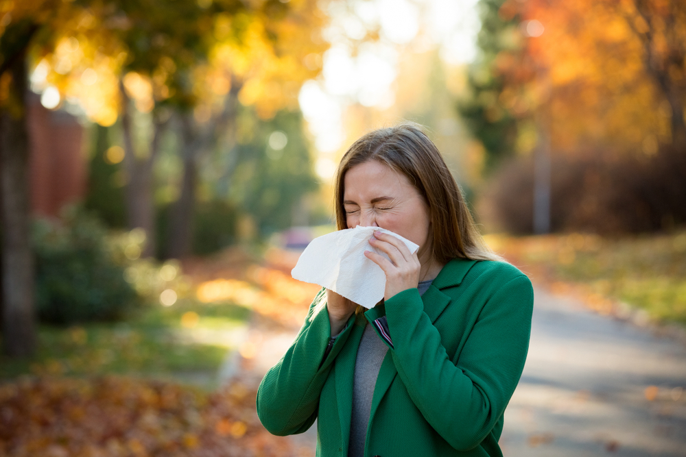 woman outside during autumn sneezing into tissue.