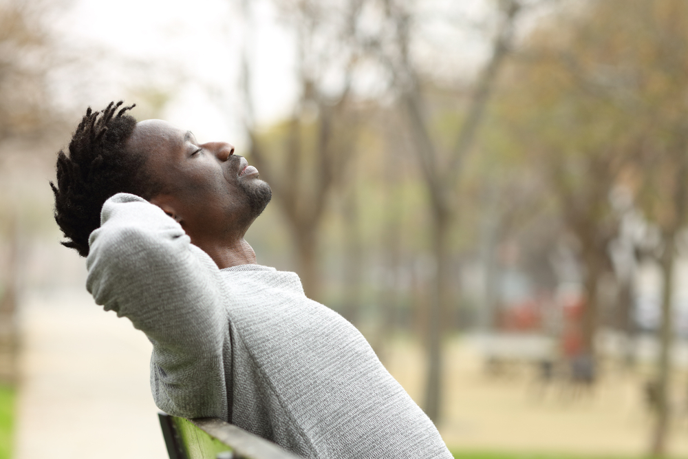 Side view portrait of a man relaxing sitting on a bench in a park.