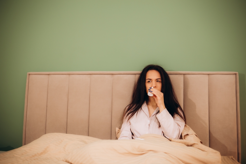 Young woman with nosebleed and tissue at home.