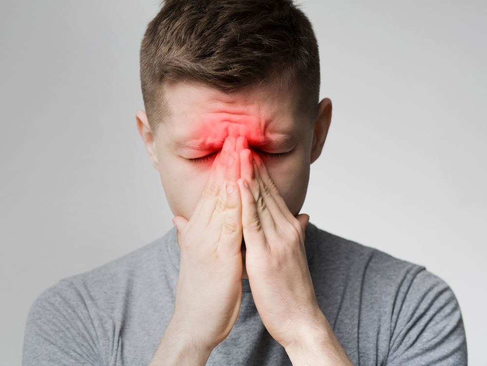 Frustrated young man suffering from sinus pressure, touching his nose with closed eyes.