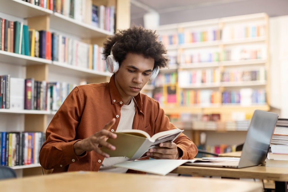 young man with headphones on studying in library.