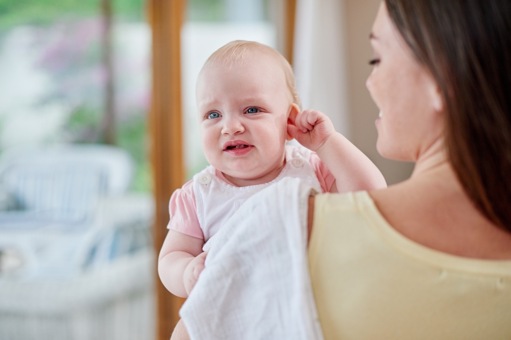 mom holding infant suffering from ear infection.