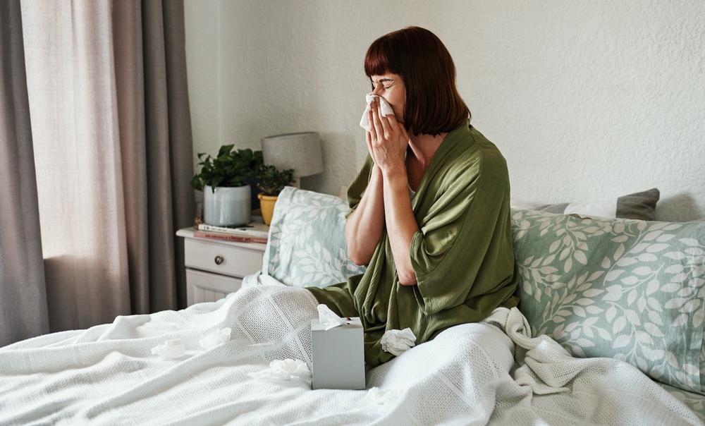 woman blowing her nose in bed due to sinus or allergies.