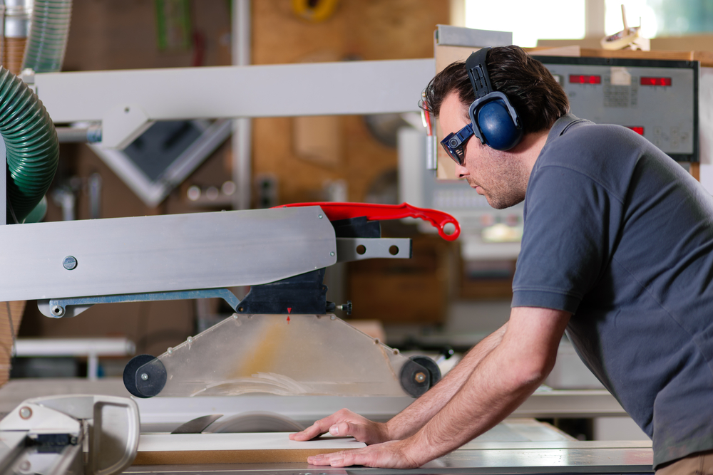 contractor using saw while wearing ear muffs and eye protection for safety.