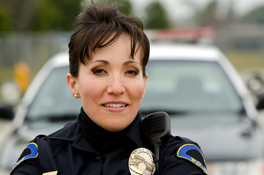 a female police officer smiling next to her police car.