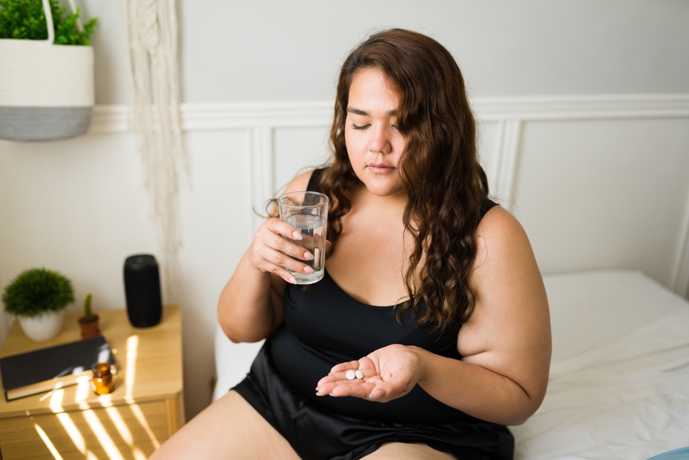 woman sitting on bed taking medications.