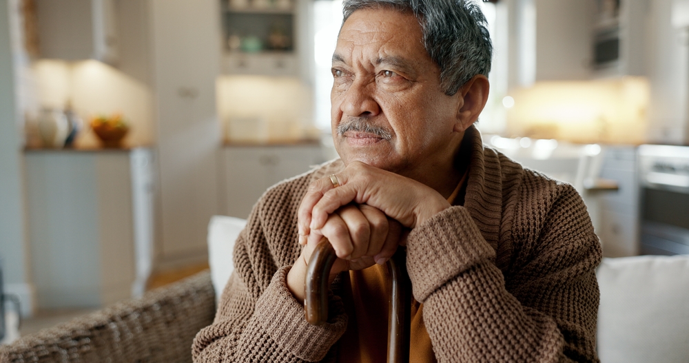 elderly person with a walking stick in a house feeling sad.